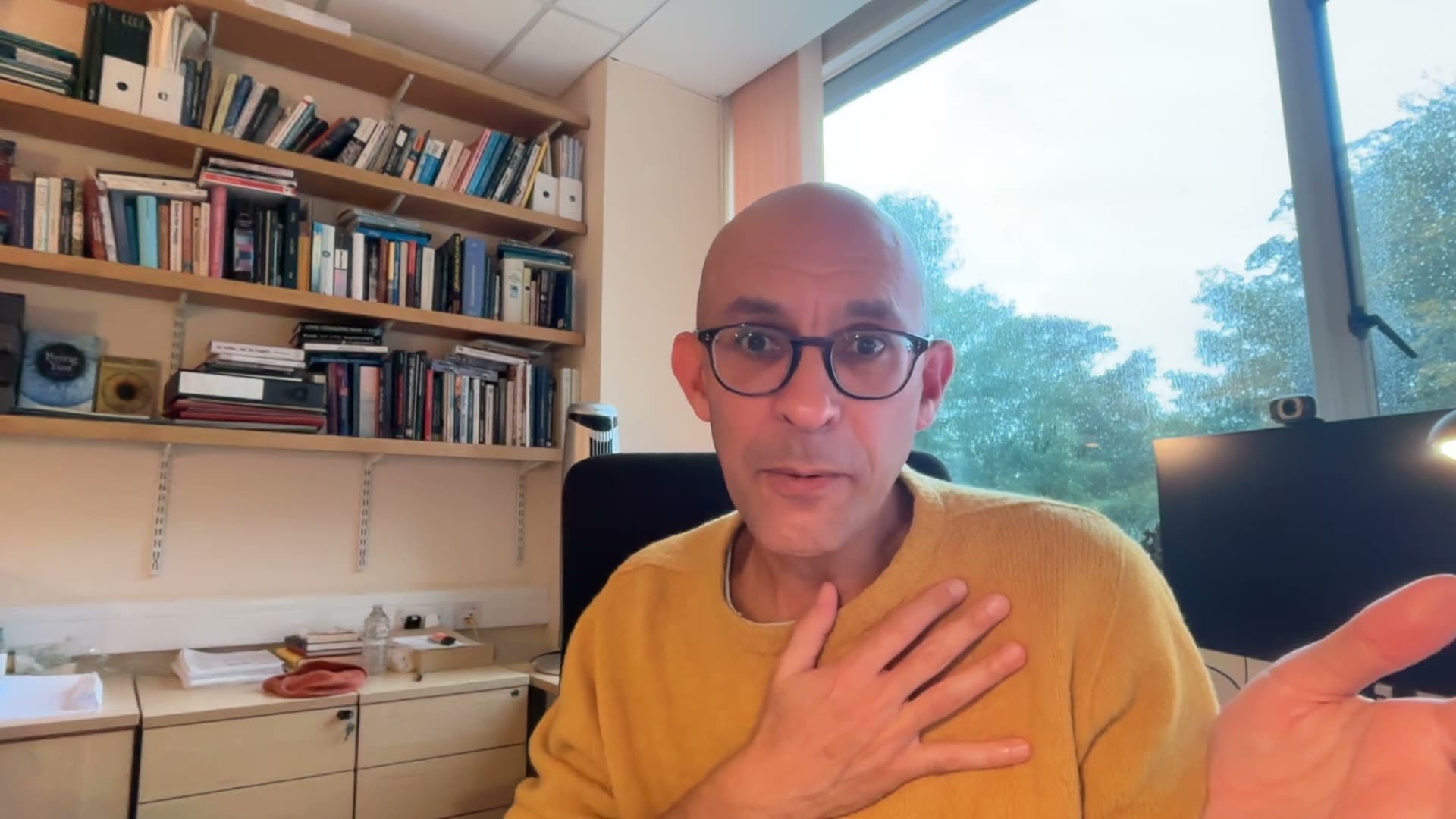 Neuroscientist Anil Seth, hand on his chest, speaking in front of a bookshelf